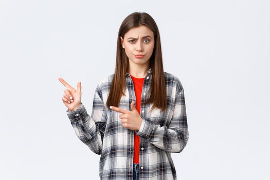 Lifestyle, different emotions, leisure activities concept. Skeptical and unimpressed girl having suspicious thoughts, express disbelief and skepticism, pointing fingers left and smirk displeased