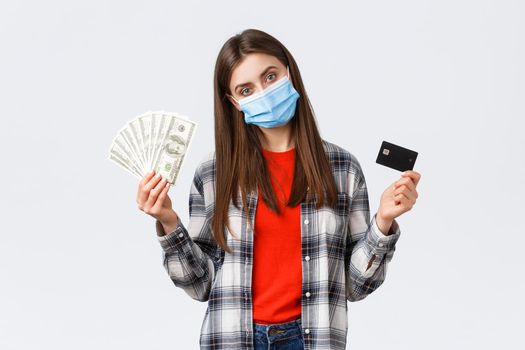 Money transfer, investment, covid-19 pandemic and working from home concept. Woman in medical mask earn cash on freelance while self-quarantine, showing dollars and credit card