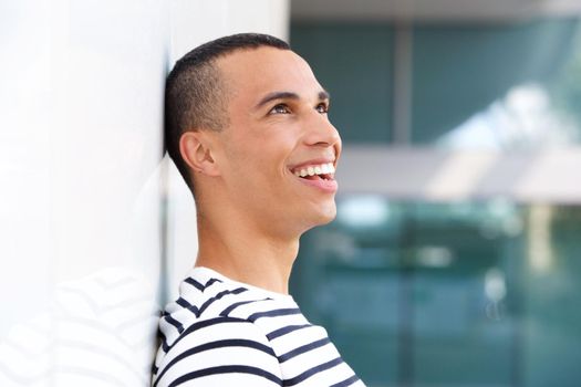 Profile happy young man leaning against white wall 