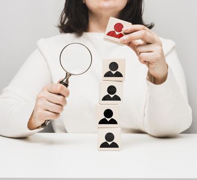 woman holding a magnifying glass and wooden cubes on a white table. Personnel recruitment concept, talented employees. Career advancement