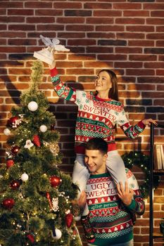 Happy couple preparing for New Year winter holidays celebration concept. Young 30s couple decorating Christmas tree create festive mood atmosphere at modern cozy house.