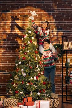 Happy couple preparing for New Year winter holidays celebration concept. Young couple decorating Christmas tree create festive mood atmosphere at modern cozy house