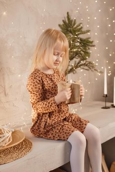 A girl is playing on Christmas Eve in a beautiful house decorated for the New Year holidays. Scandinavian-style interior with live fir trees and a wooden staircase.