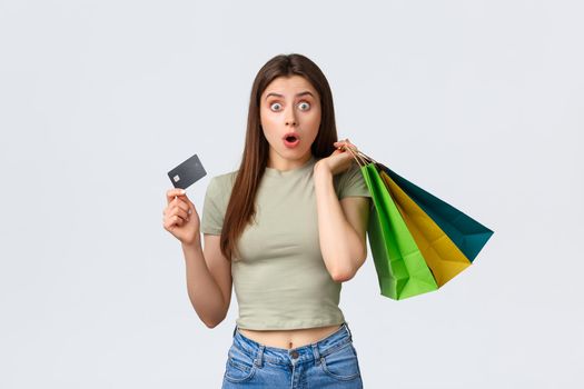 Shopping mall, lifestyle and fashion concept. Shocked and impressed woman with credit card buying new clothes, seeing special discount, hurry up to cashier with bags