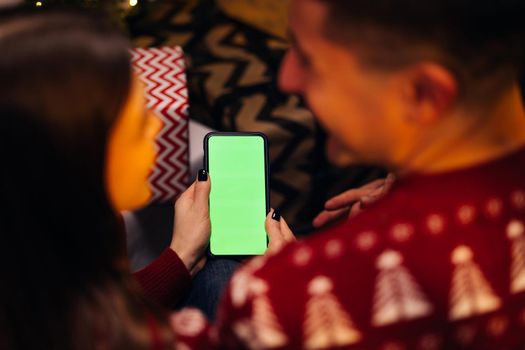 Caucasian couple using smartphone for christmas video call with green mock up screen. Christmas, festivity and communication technology