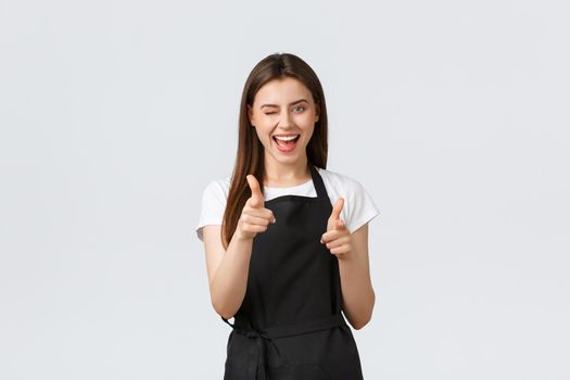 Grocery store employees, small business and coffee shops concept. Excited cheeky barista in black apron pointing fingers camera, congratulate person, saying well played