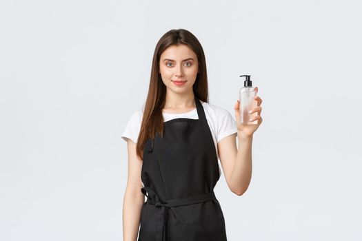 Grocery store employees, small business and coffee shops concept. Friendly-looking pleasant restaurant worker in black apron showing hand sanitizer, assure all prevenive measures are done