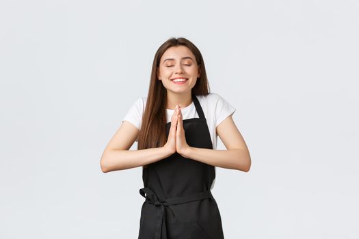 Grocery store employees, small business and coffee shops concept. Hopeful cheerful and optimistic barista making wish, hold hands in pray, praying and smiling happy
