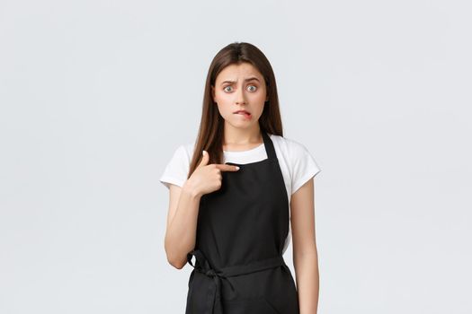Grocery store employees, small business and coffee shops concept. Embarrassed and worried female barista in black apron biting lip and looking anxious, pointing herself
