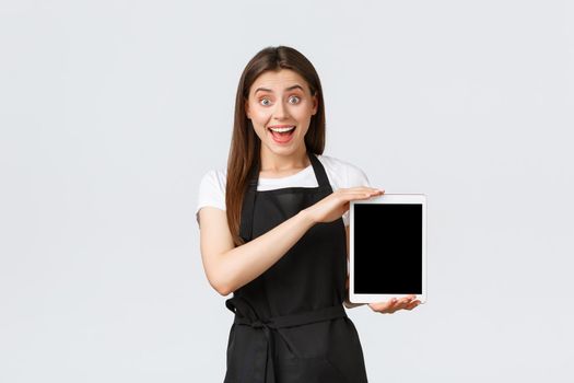 Grocery store employees, small business and coffee shops concept. Excited saleswoman showing cool advertisement, smiling amazed as show digital tablet display, stand white background