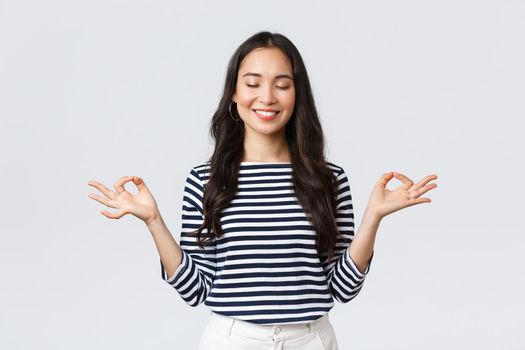 Lifestyle, people emotions and casual concept. Calm happy young woman feeling peaceful during meditation, close eyes and smiling as hold hands in zen nirvana gesture, do yoga exercise