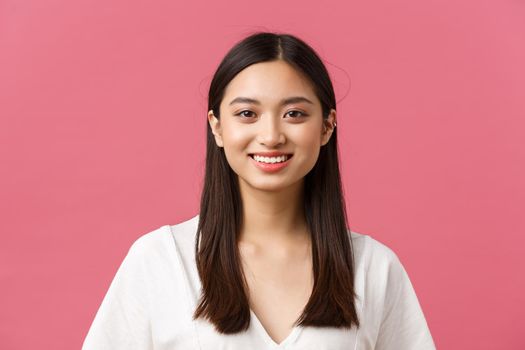 Beauty products advertisement, haircare and women fashion concept. Close-up of cute romantic silly asian girl with medium dark haircut, smiling white teeth with happy expression, pink background