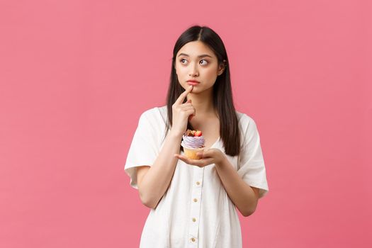 Food, cafe and restaurants, summer lifestyle concept. Thoughtful cute hesitant asian woman looking away doubtful, thinking about calories as staying on diet, tempting to eat delicious dessert