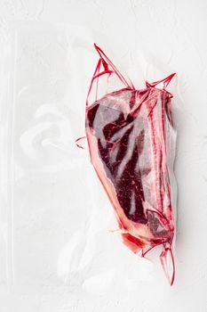 Dry aged beef marbled meat, raw fresh club beefsteak in plastic package, on white stone surface, top view flat lay