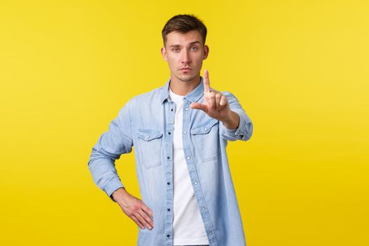 Lifestyle, people emotions and summer leisure concept. Serious gay man in casual outfit, shaking finger in prohibition, disapprove and trying stop person, give restriction over yellow background