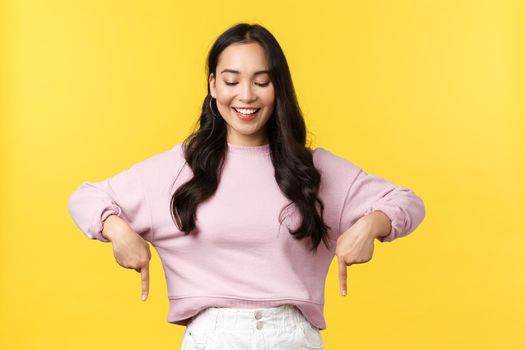 People emotions, lifestyle and fashion concept. Cheerful beautiful young 20s asian woman in stylish outfit introduce new promo, pointing fingers down and smiling happy at advertisement