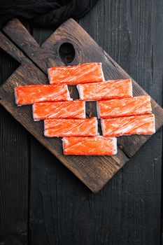 Fresh Crab meat stick surimi , on wooden cutting board, on black wooden table background, top view flat lay