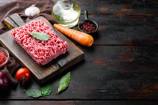 Ingredients for cooking Bolognese sauce, minced beef meat tomatoe and herbs, on wooden cutting board, on old dark wooden table background, with copy space for text