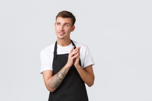 Small business owners, coffee shop and staff concept. Creative and smart handsome sly barista, waiter or cafe employee in black apron, steeple fingers and smirk, have genius idea, white background