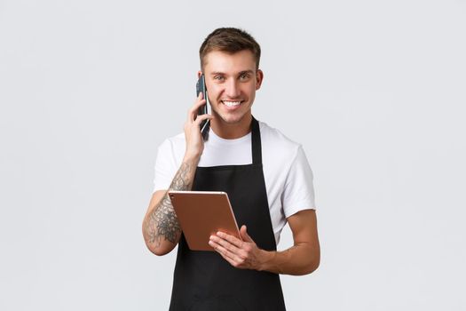 Retail stores, small business, cafe and restaurants takeaway concept. Handsome smiling salesman, barista talking on phone, laughing happy, taking order for delivery, holding digital tablet