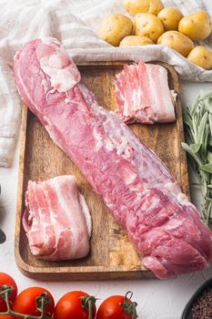 Raw pork loin with ingredients and herbs for baking, sage, potatoe, on wooden tray, on white stone background