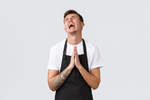 Employees, grocery stores and coffee shop concept. Hopeless barista in despair praying, screaming distressed, holding hands in plead, begging for something, standing white background