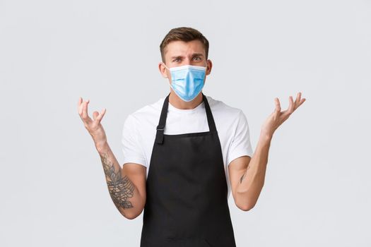 Coronavirus, social distancing in cafes and restaurants, business during pandemic concept. Frustrated complaining barista in medical mask shaking hands and raise them disappointed, arguing