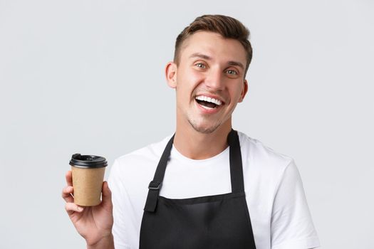 Cafe and restaurants, coffee shop owners and retail concept. Friendly joyful handsome barista in black apron laughing pleasant and handing over takeaway order, standing white background