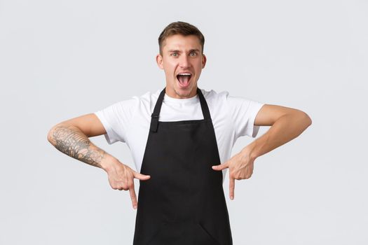 Small business owners, coffee shop and staff concept. Cheerful enthusiastic handsome barista inviting guests to special summer menu, pointing fingers down encourage click link