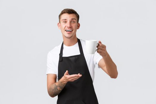 Small business, coffee shop, cafe and restaurants concept. Friendly handsome waiter, barista selling drink, handing guest cappuccino in mug, smiling happy, white background