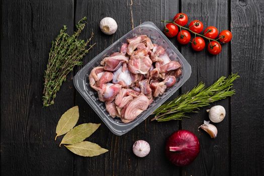 Heap of raw poultry stomachs in plastic pack, on black wooden table background, top view flat lay