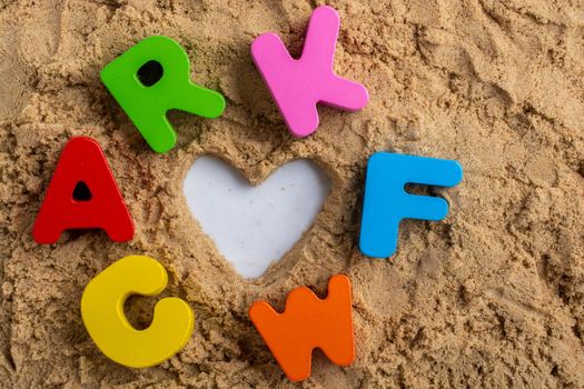 Heart shape and colorful Letters placed on sand