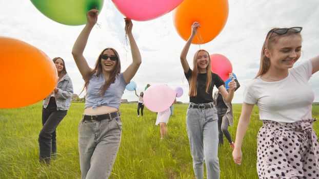 Girls friends are walking across the field with large balloons and colorful balloons.