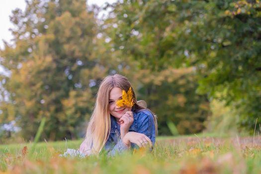 A young girl lies on the grass in a warm autumn in the evening with a petal in her hands.