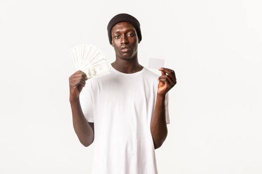 Unbothered cool african-american rich guy showing money and credit card, white background