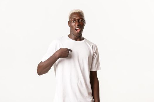 Portrait of sassy african-american blond man, pointing at himself and swearing, standing white background arrogant