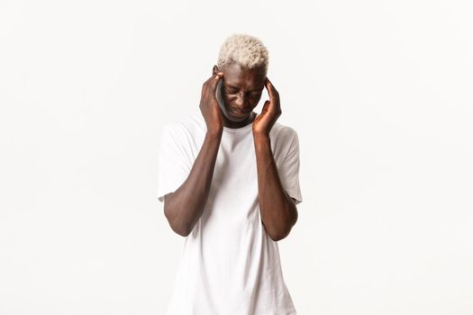 Portrait of dizzy african-american blond man, feeling headache, grimacing and bending from pain, having migraine, standing white background