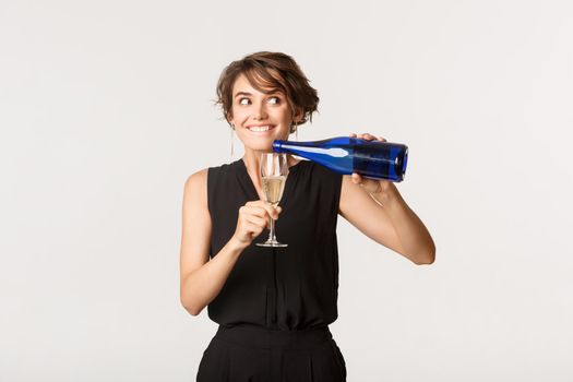 Cunning party girl pouring herself glass of champagne and smiling excited