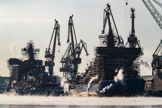 The construction of nuclear icebreakers, cranes of of the Baltic shipyard in a frosty winter day, steam over the Neva river, smooth surface of the river