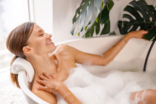 Smiling young woman enjoying bathing while relaxing in the bathtub at luxury spa resort