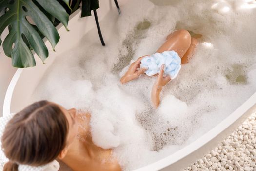 High angle view of relaxed woman lying down in the tub with foam, spending time at luxury spa resort