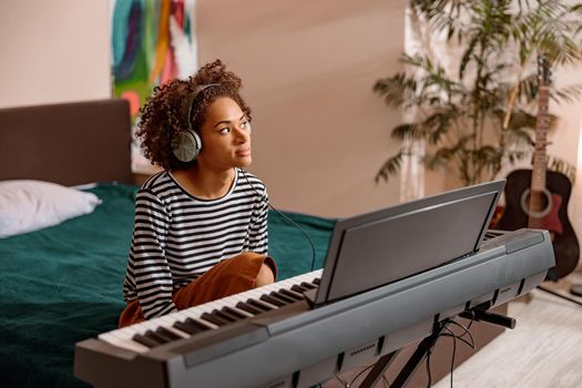 Multiracial woman sitting near synthesizer at home
