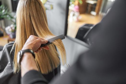 Hairdresser is choping hair of blonde woman is salon