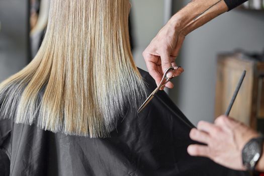Hairdresser is choping hair of blonde woman is salon