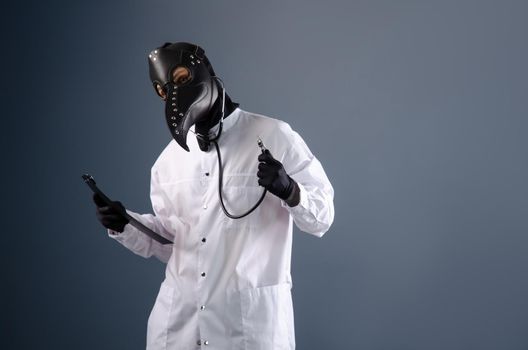 a doctor in a dressing gown wearing a plague doctor mask with a stethoscope in his hands