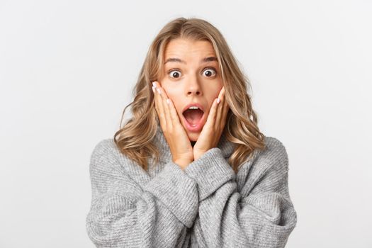 Close-up of blond pretty girl looking surprised, scream of amazement, standing over white background