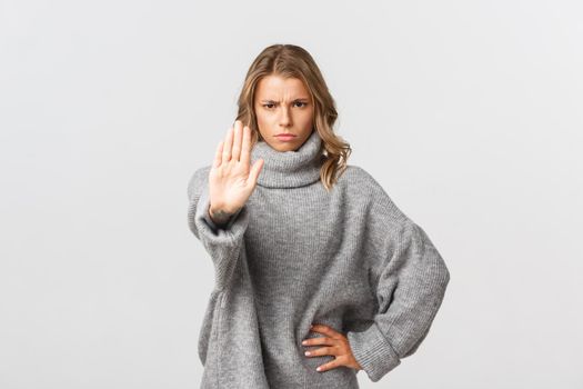 Serious confident woman in grey sweater, extend one arm and telling to stop, prohibit action, frowning disappointed, standing over white background