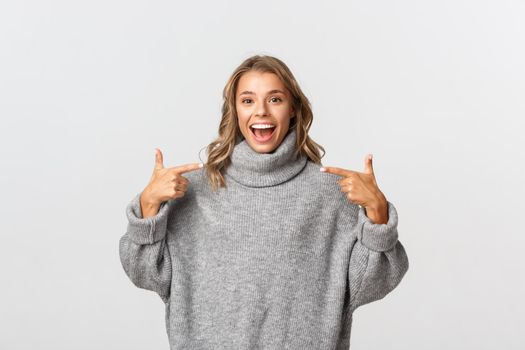 Attractive happy woman in casual clothing pointing at your logo and smiling, standing over white background