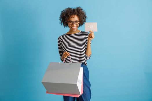 Joyful young woman holding purchases and gift card