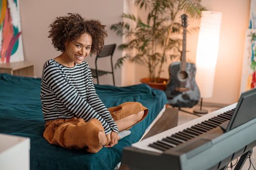 Joyful female musician sitting near synthesizer at home